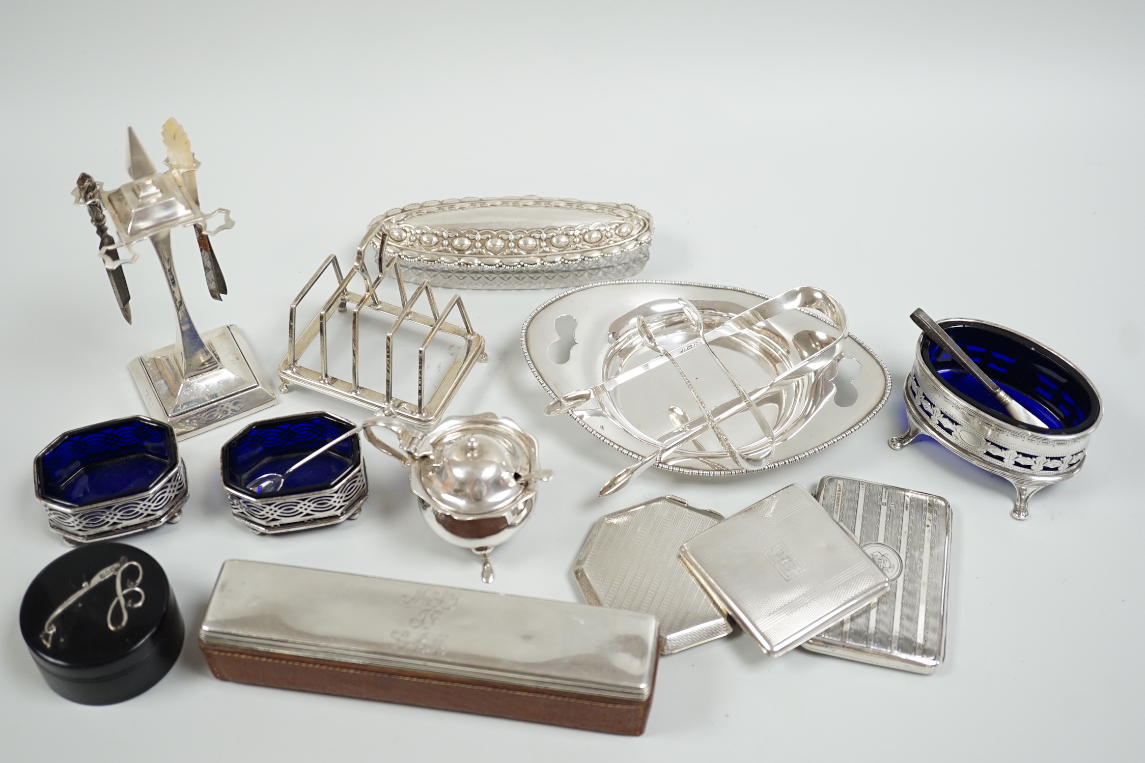 A group of mixed silver ware including a manicure stand, toastrack, purse, two compacts, four condiments, two pairs of sugar tongs, a stand and two mounted glass toilet jars.